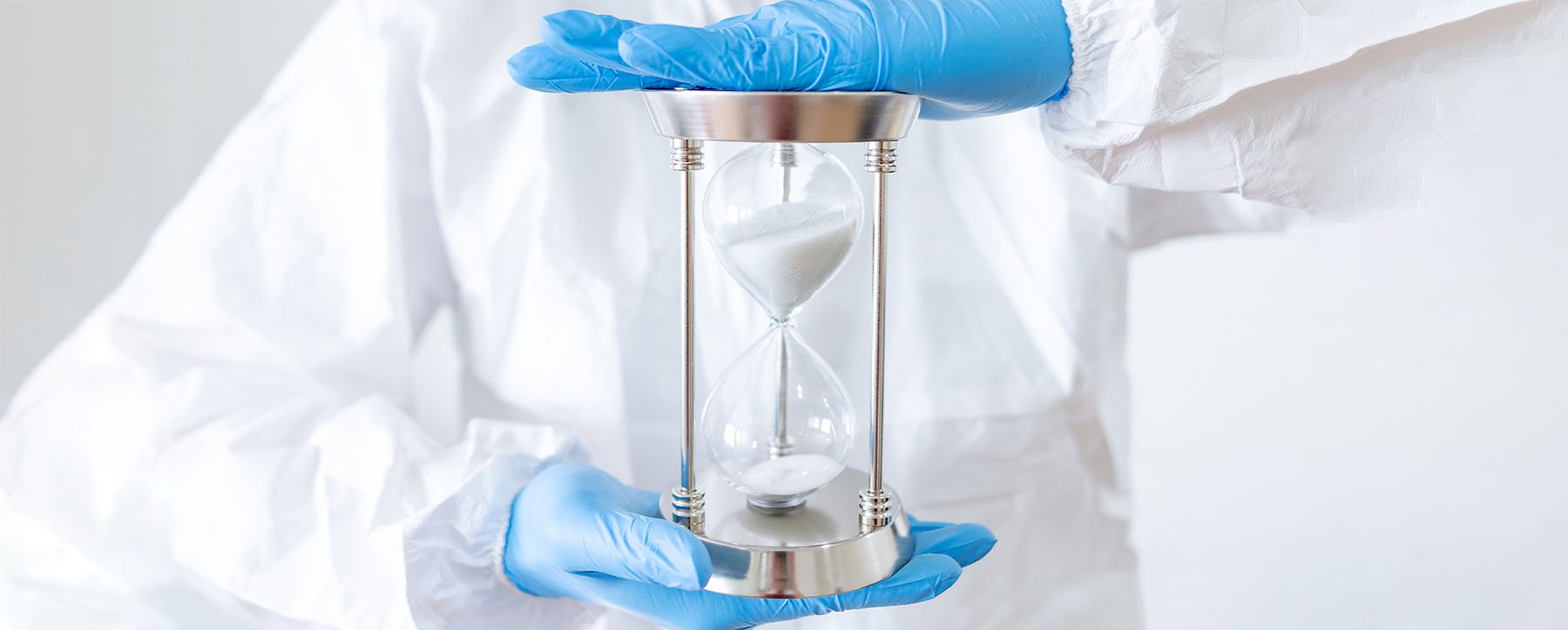 An allied health worker in blue gloves holds an hourglass