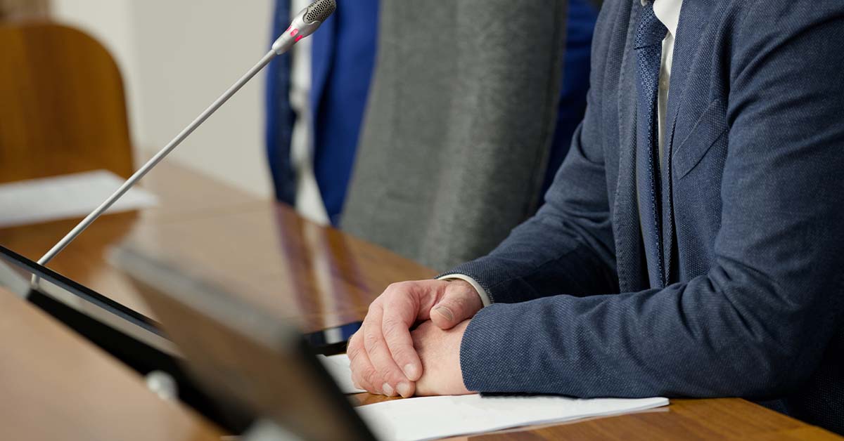 A speaker clasps his hands on a desk in a government building