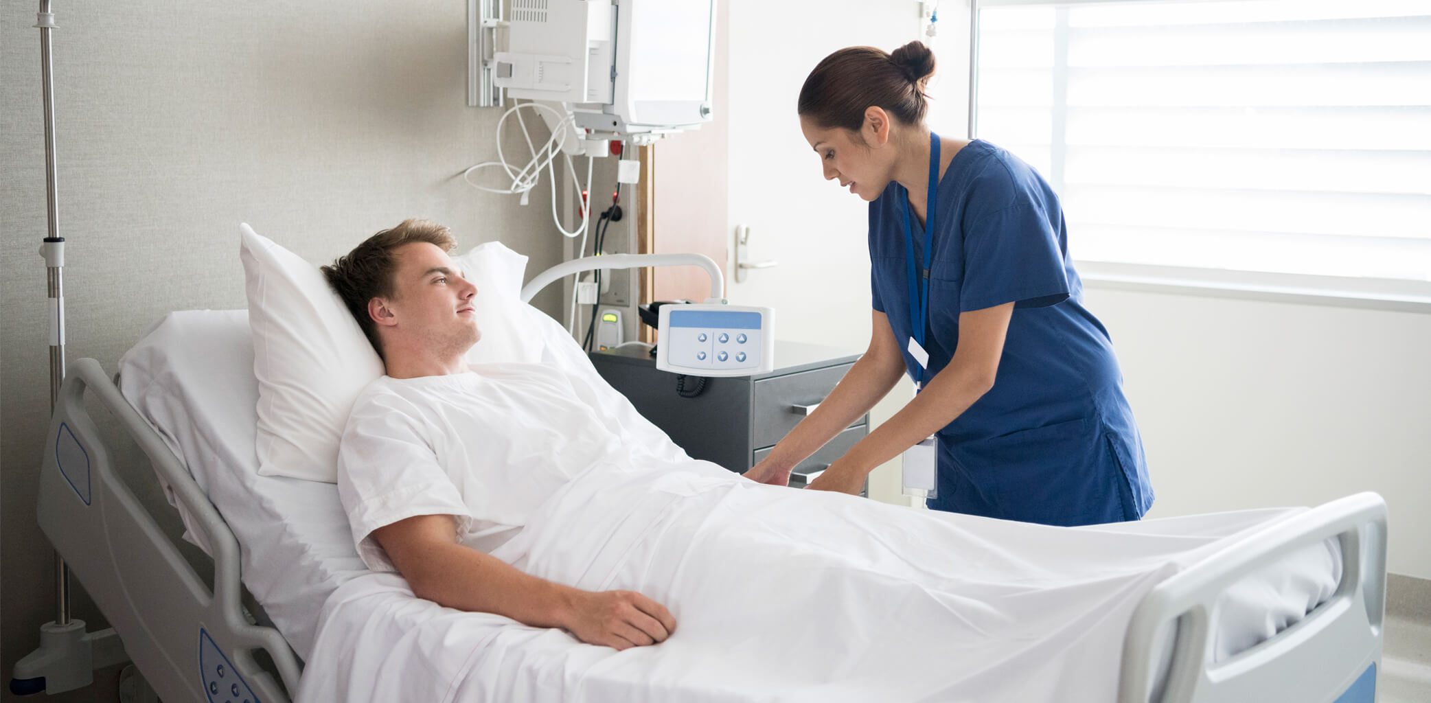 A patient care technician is working to make a patient comfortable in a hospital bed