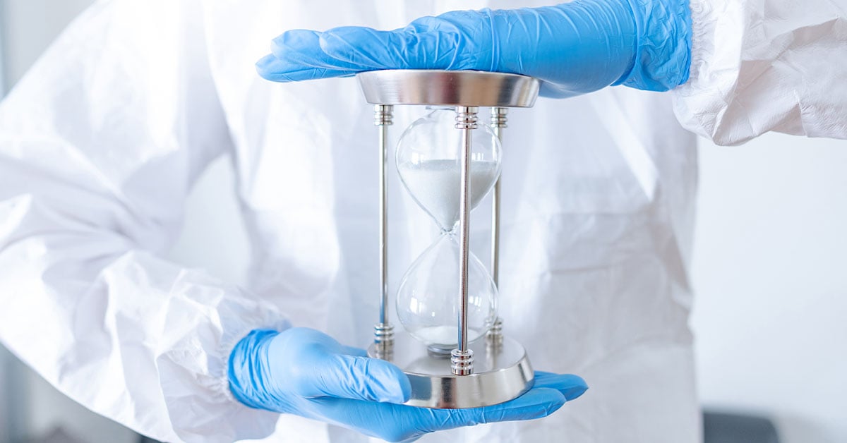 An allied health worker holds an hourglass in gloved hands